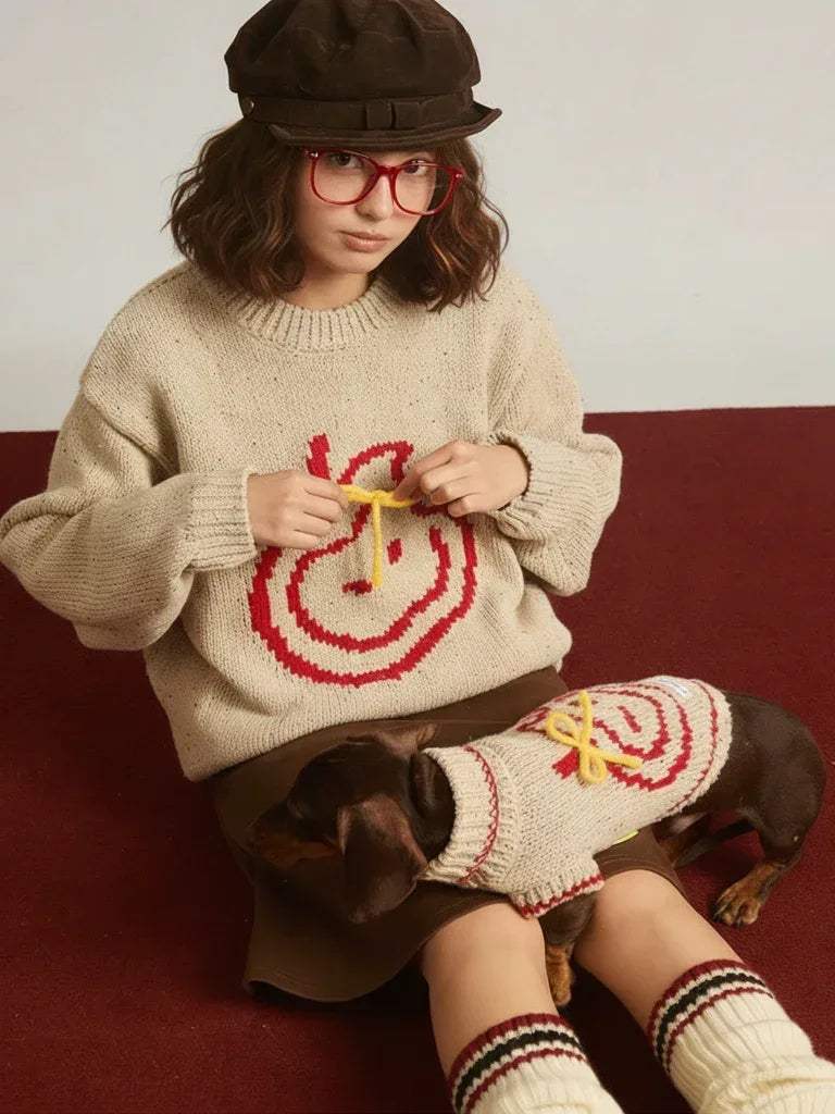 Woman wearing a sweater with a dog wearing a matching sweater, both sitting on a red surface.