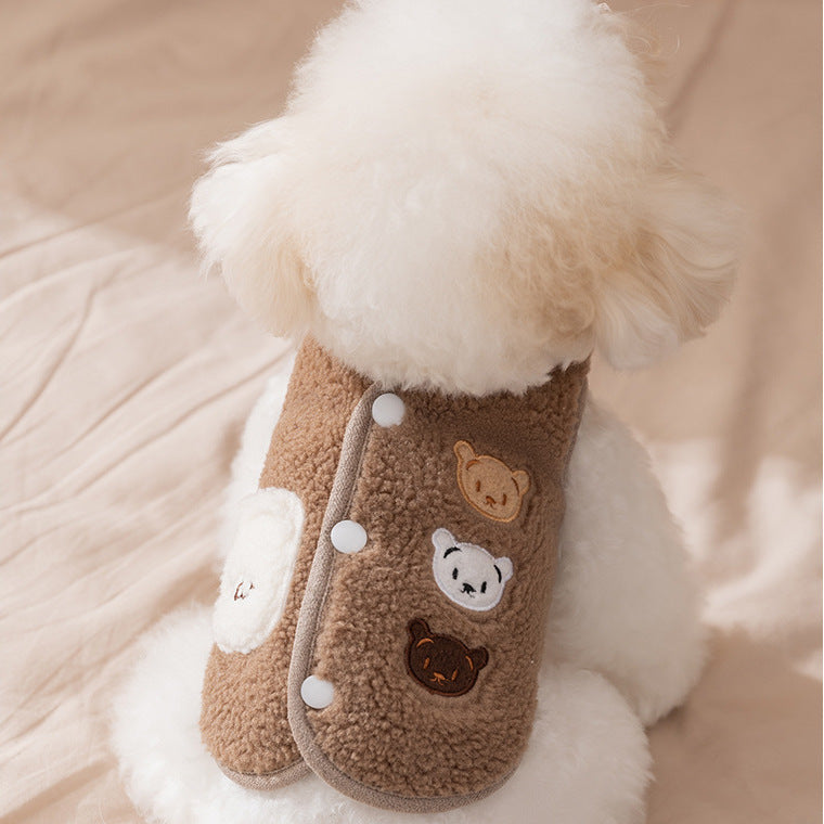 Small white dog wearing a brown jacket with a bear design on a beige background