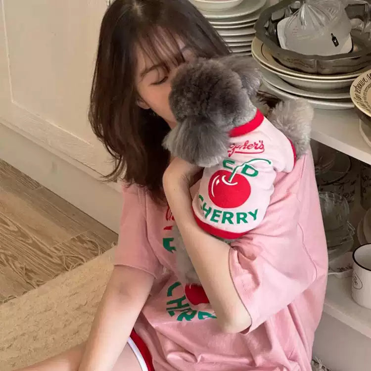 Woman holding a small dog wearing a 'Cherry' themed outfit in a kitchen setting.