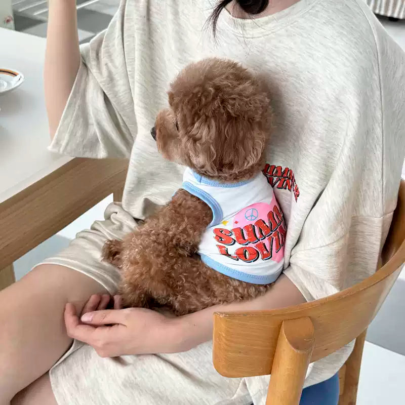 Person holding a small brown dog in a white shirt with colorful text