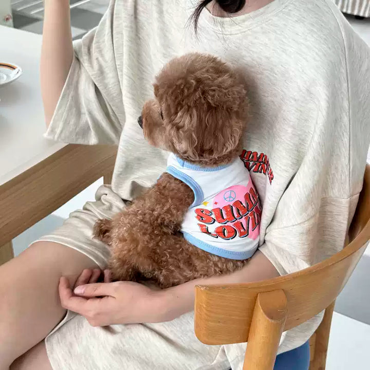 Person holding a small brown dog in a white shirt with colorful text