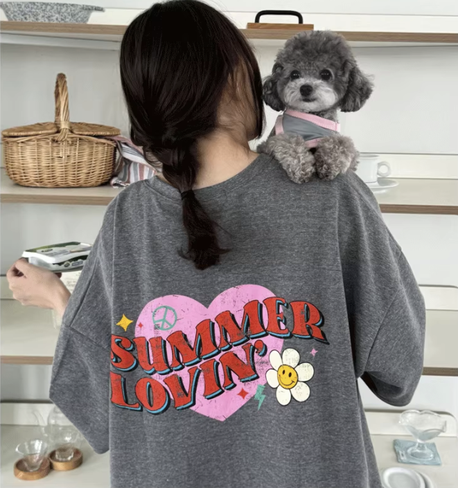 Person wearing a gray t-shirt with 'Summer Lovin'' design, holding a small dog.