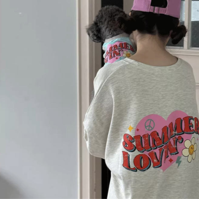 Person wearing a 'Summer Lovin'' shirt with a dog on her shoulder, standing indoors.