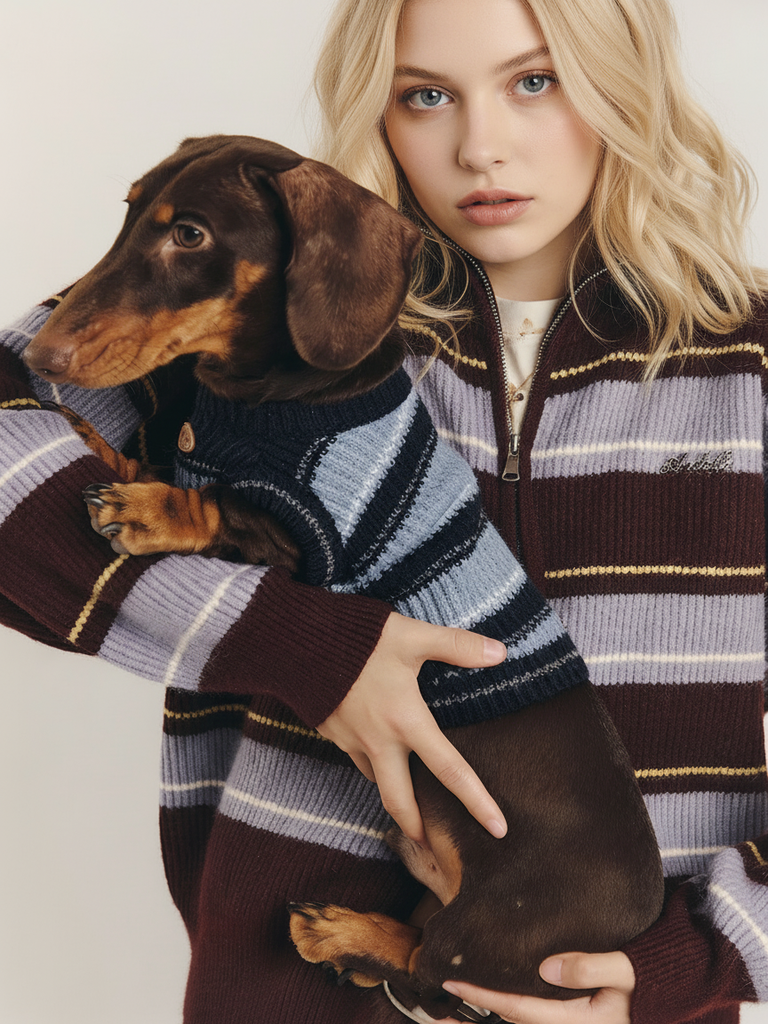 Woman holding a dachshund, both wearing matching striped sweaters, against a white background