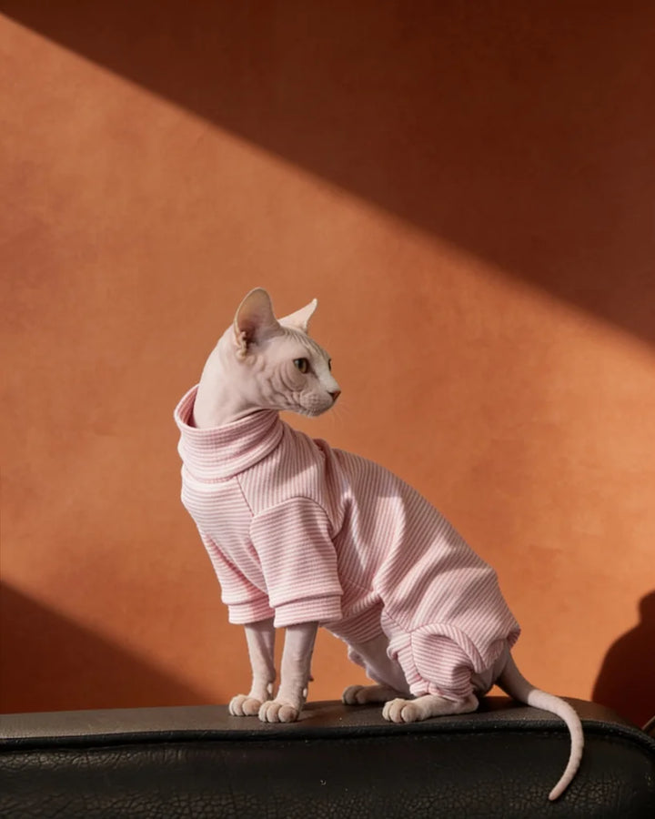 A hairless cat wearing a light pink ribbed turtleneck onesie