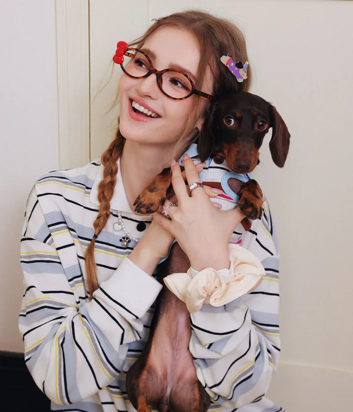 A woman holding a small dog, both wearing striped shirts