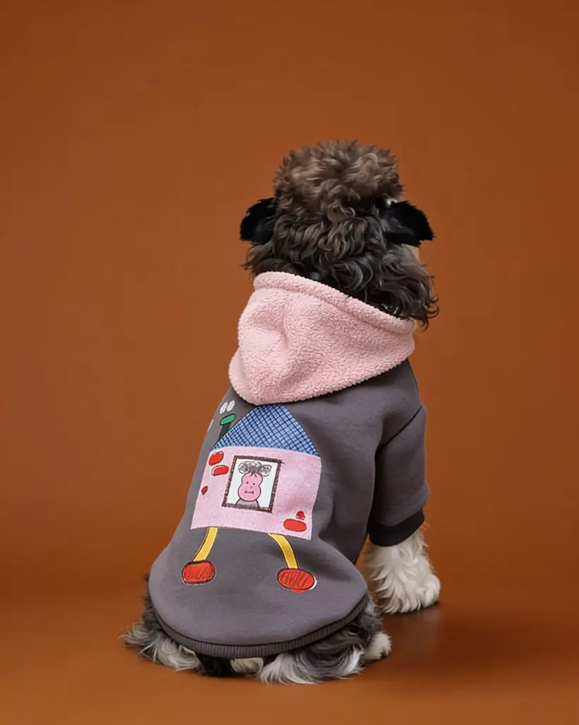 A small gray and white dog wearing a gray hoodie with a pink hood and a cartoon house